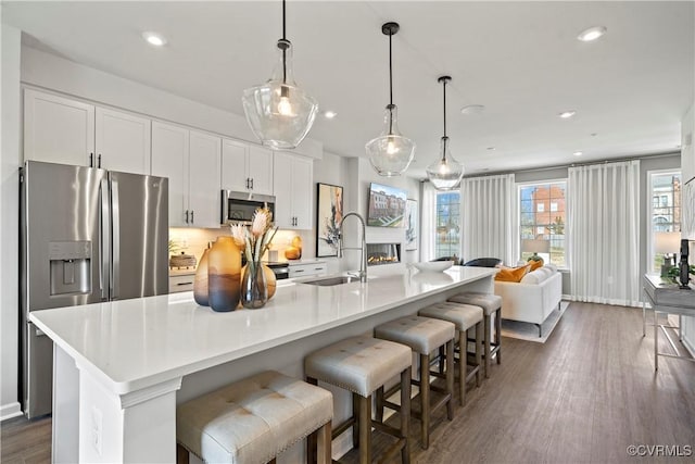 kitchen featuring a sink, stainless steel appliances, a kitchen island with sink, dark wood finished floors, and white cabinets