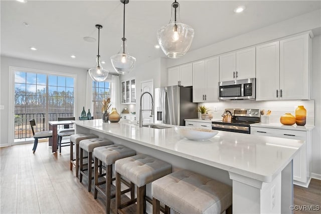 kitchen with a sink, a kitchen island with sink, white cabinetry, backsplash, and appliances with stainless steel finishes