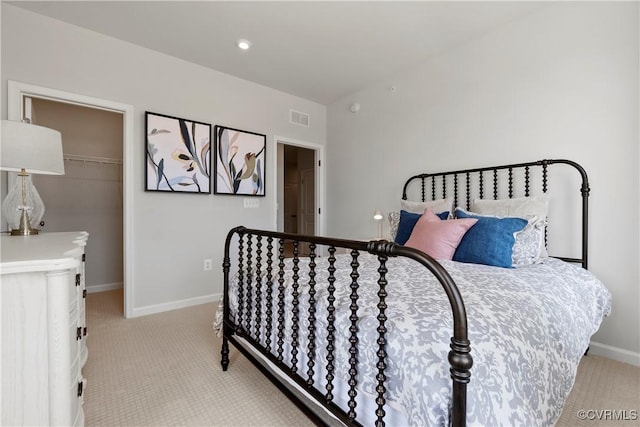 bedroom with light carpet, baseboards, and a walk in closet