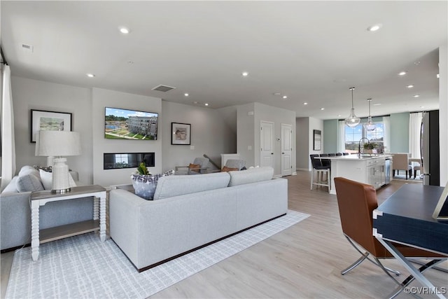 living room with light wood finished floors, visible vents, baseboards, and recessed lighting
