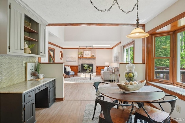 dining room with a wainscoted wall, light wood-type flooring, a brick fireplace, and ornamental molding