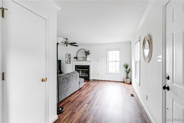foyer featuring wood finished floors, a ceiling fan, crown molding, a glass covered fireplace, and baseboards