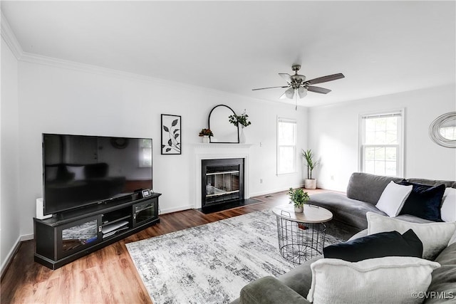living area featuring a ceiling fan, wood finished floors, crown molding, a fireplace with flush hearth, and baseboards