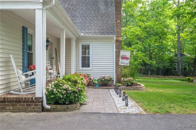 entrance to property featuring roof with shingles, a chimney, and a yard