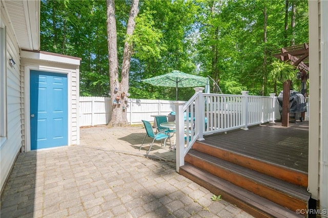 view of patio with a wooden deck, a fenced backyard, grilling area, outdoor dining area, and view of wooded area