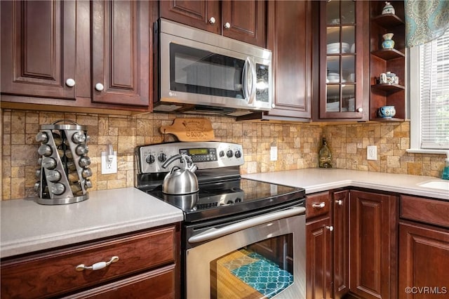 kitchen featuring appliances with stainless steel finishes, backsplash, light countertops, open shelves, and glass insert cabinets