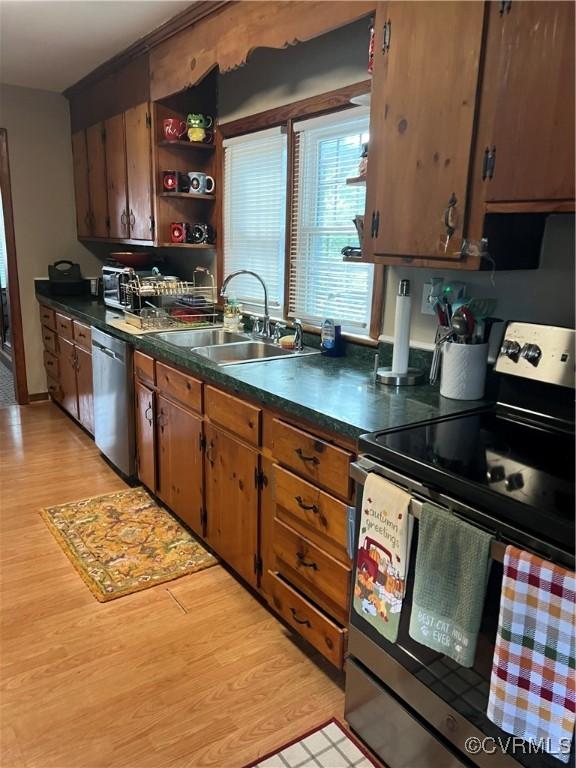 kitchen featuring stainless steel appliances, a sink, dark countertops, and light wood-style flooring