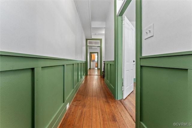 hallway with hardwood / wood-style floors, a decorative wall, and a wainscoted wall