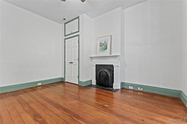 unfurnished living room with hardwood / wood-style floors, a fireplace with flush hearth, a ceiling fan, and baseboards