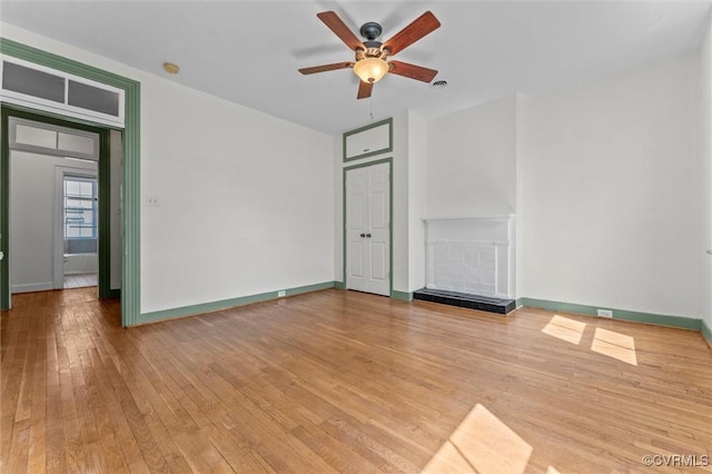 unfurnished bedroom featuring wood-type flooring, baseboards, a ceiling fan, and a tiled fireplace