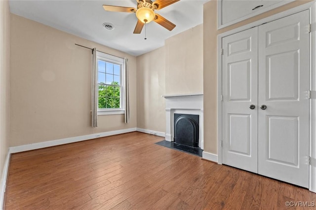 unfurnished living room with a ceiling fan, baseboards, wood finished floors, and a fireplace with flush hearth