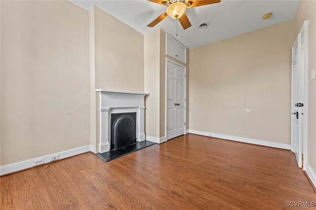 unfurnished living room featuring ceiling fan, wood finished floors, baseboards, and a fireplace with raised hearth
