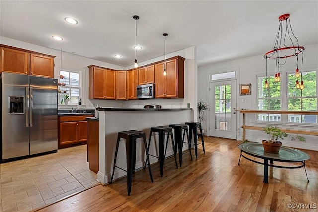 kitchen with appliances with stainless steel finishes, dark countertops, brown cabinetry, a kitchen breakfast bar, and recessed lighting