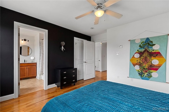 bedroom featuring light wood-style floors, baseboards, ceiling fan, and ensuite bathroom