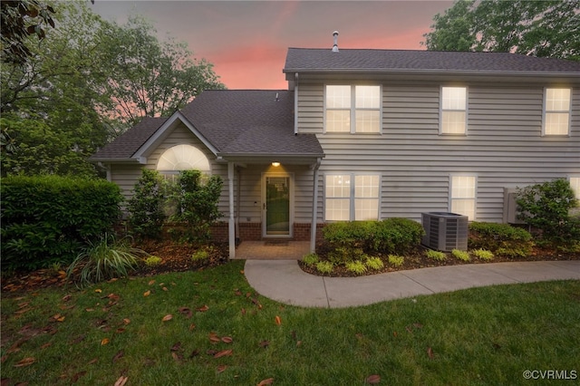 traditional-style home with central air condition unit, a front lawn, brick siding, and a shingled roof