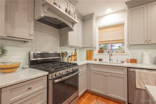 kitchen with appliances with stainless steel finishes, a sink, under cabinet range hood, backsplash, and light stone counters