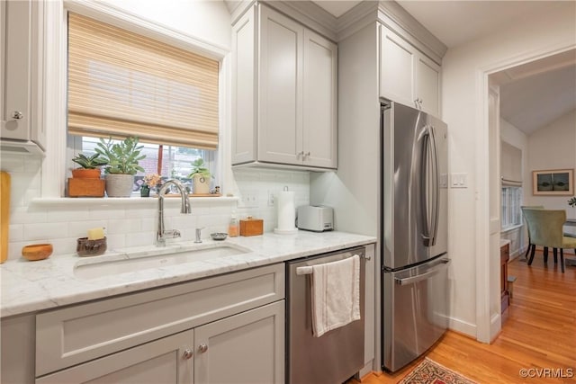 kitchen featuring stainless steel appliances, a sink, light wood-style flooring, decorative backsplash, and light stone countertops