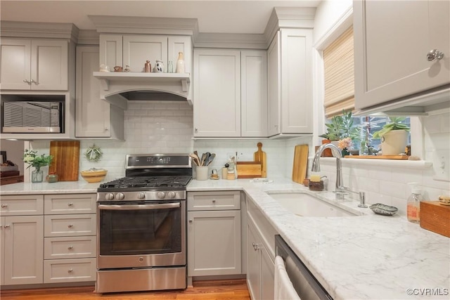 kitchen featuring stainless steel appliances, a sink, tasteful backsplash, and light stone counters