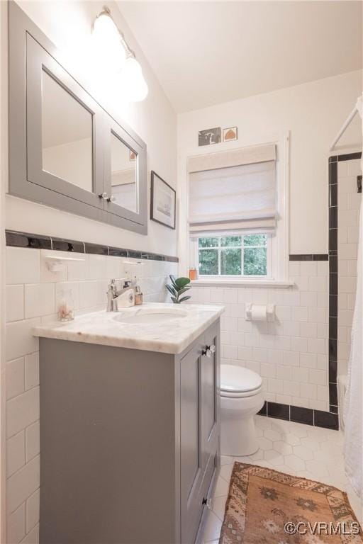 bathroom featuring tile walls, tile patterned flooring, toilet, vanity, and a wainscoted wall