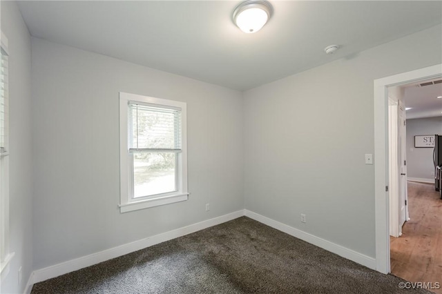 unfurnished room with a smoke detector, baseboards, and dark colored carpet
