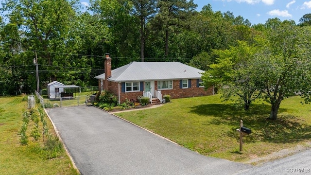 view of front of property featuring asphalt driveway, a chimney, brick siding, an outdoor structure, and a storage shed