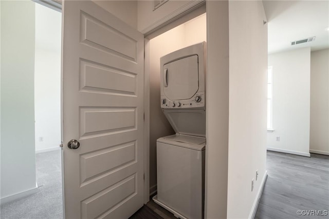 washroom with stacked washer / drying machine, baseboards, and wood finished floors