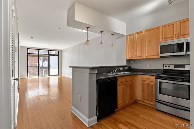 kitchen with stainless steel appliances, a sink, dark countertops, open floor plan, and light wood-style floors