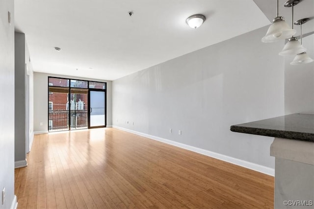 unfurnished living room with light wood finished floors, baseboards, and floor to ceiling windows