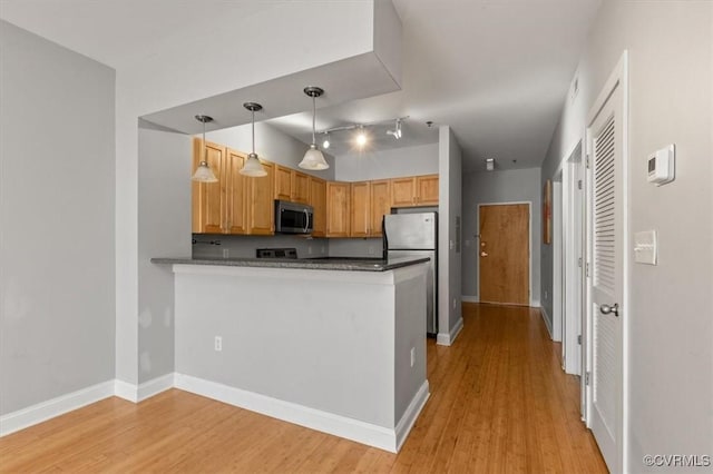 kitchen featuring appliances with stainless steel finishes, light wood-style floors, a peninsula, pendant lighting, and dark countertops