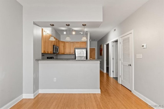 kitchen featuring appliances with stainless steel finishes, light wood-style flooring, a peninsula, and hanging light fixtures