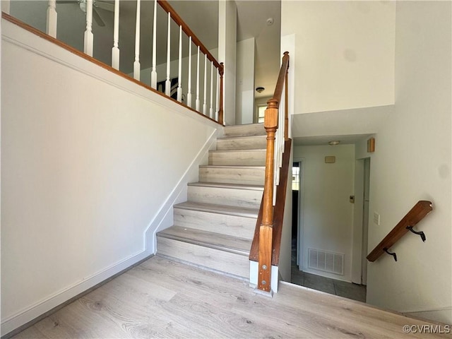 staircase with wood finished floors, a high ceiling, and baseboards