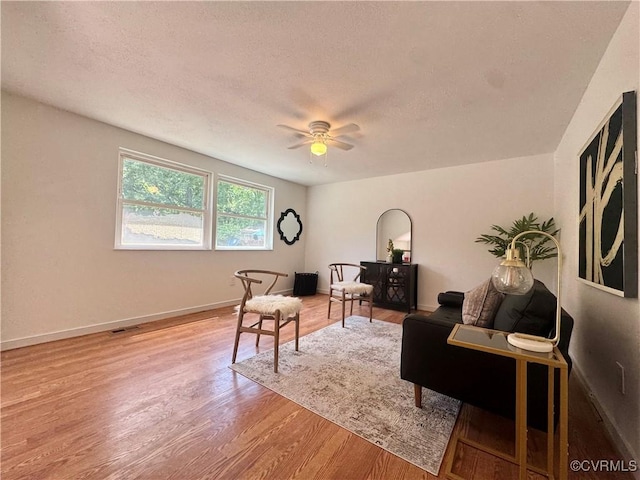 living area featuring light wood finished floors, a textured ceiling, ceiling fan, and baseboards