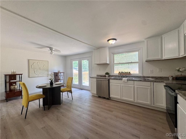 kitchen featuring black electric range, dishwasher, a sink, light wood-style floors, and dark countertops