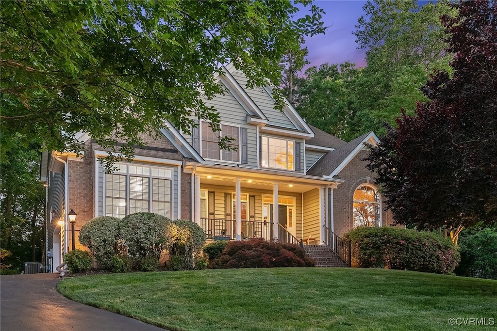 craftsman-style home with covered porch, a lawn, central air condition unit, and brick siding