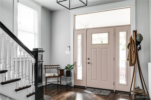 foyer entrance with dark wood finished floors, stairway, and healthy amount of natural light