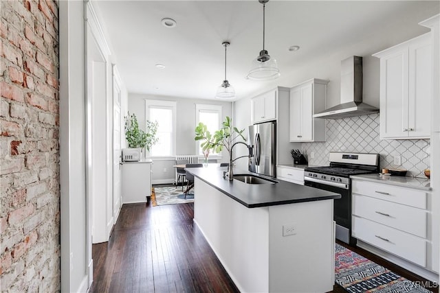 kitchen featuring stainless steel appliances, wall chimney range hood, a sink, dark wood-type flooring, and a kitchen island with sink