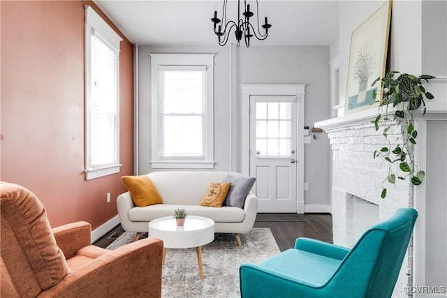 living area featuring a fireplace, dark wood-type flooring, a chandelier, and baseboards