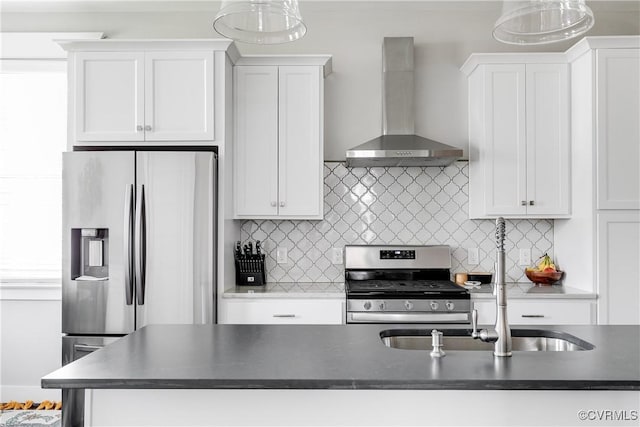 kitchen with wall chimney exhaust hood, stainless steel appliances, dark countertops, white cabinetry, and a sink