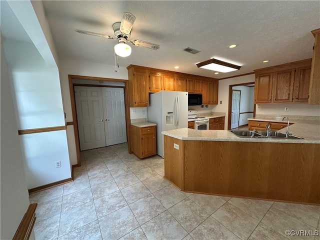 kitchen featuring white appliances, a sink, brown cabinets, a peninsula, and recessed lighting