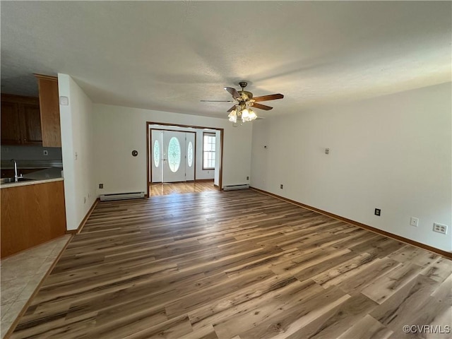 unfurnished living room with a baseboard heating unit, a sink, light wood-style floors, and a ceiling fan