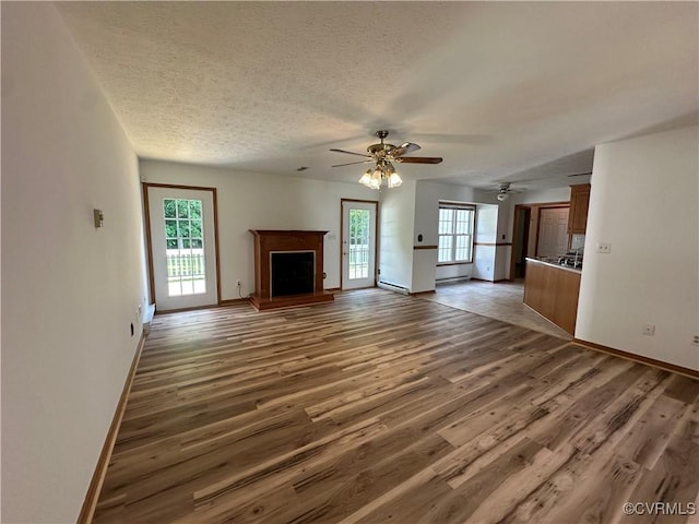 unfurnished living room featuring wood finished floors, baseboards, ceiling fan, a textured ceiling, and baseboard heating