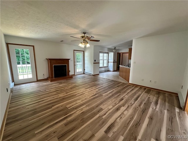 unfurnished living room with a ceiling fan, baseboards, light wood finished floors, a fireplace with raised hearth, and a textured ceiling