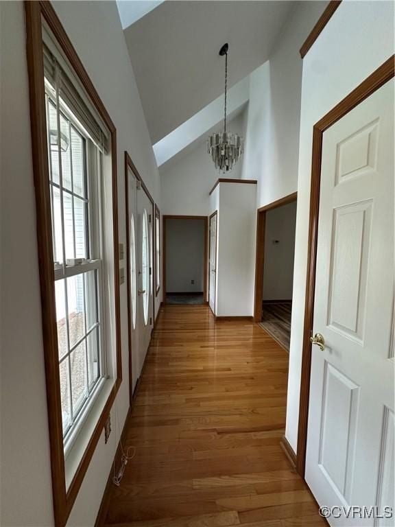 hallway featuring a chandelier, healthy amount of natural light, light wood finished floors, and high vaulted ceiling