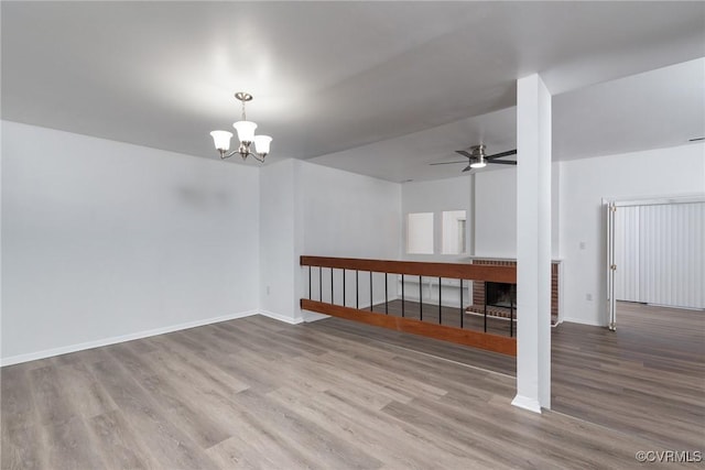 spare room featuring wood finished floors, ceiling fan, a chandelier, and baseboards