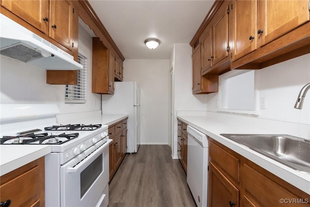 kitchen with white appliances, under cabinet range hood, a sink, brown cabinetry, and wood finished floors