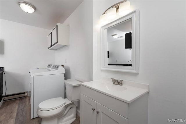 half bath with washing machine and dryer, baseboard heating, wood finished floors, vanity, and toilet