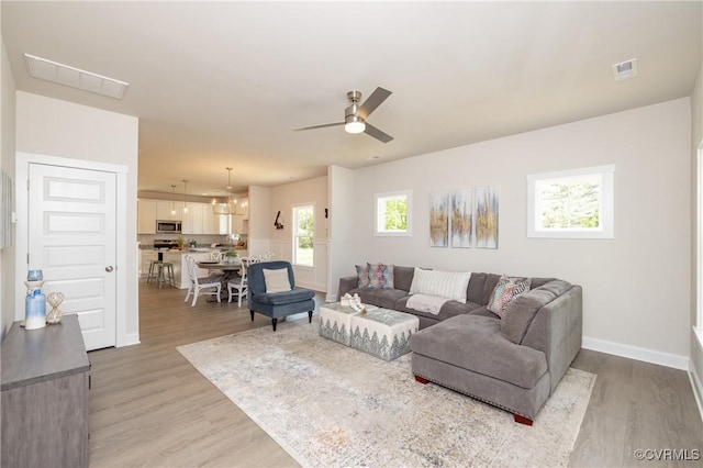 living room with light wood finished floors, ceiling fan, and baseboards