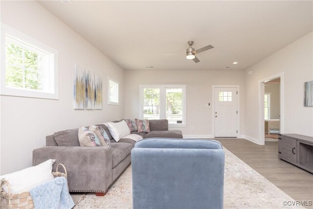 living area with light wood finished floors, a ceiling fan, and baseboards