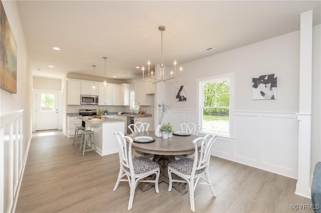 dining space featuring plenty of natural light, light wood-type flooring, wainscoting, a chandelier, and a decorative wall