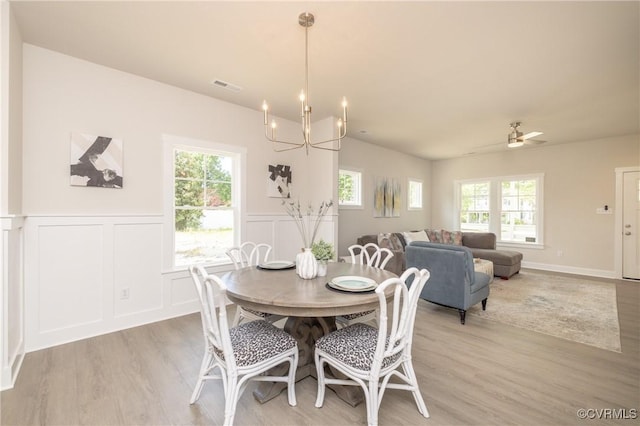 dining area featuring light wood-type flooring, a chandelier, a decorative wall, and a wainscoted wall